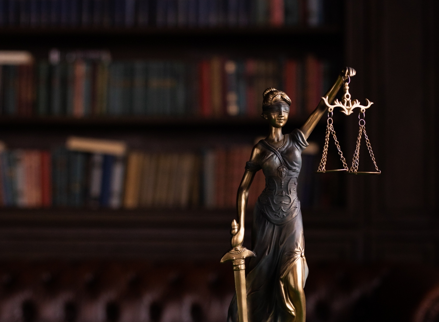 Statue of Lady Justice holding scales, with a blurred background of bookshelves.