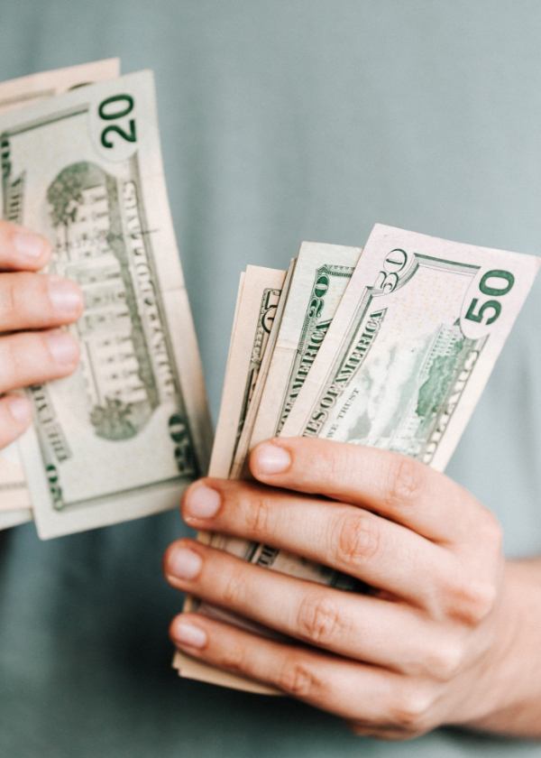 Person holding and counting a stack of U.S. dollar bills.