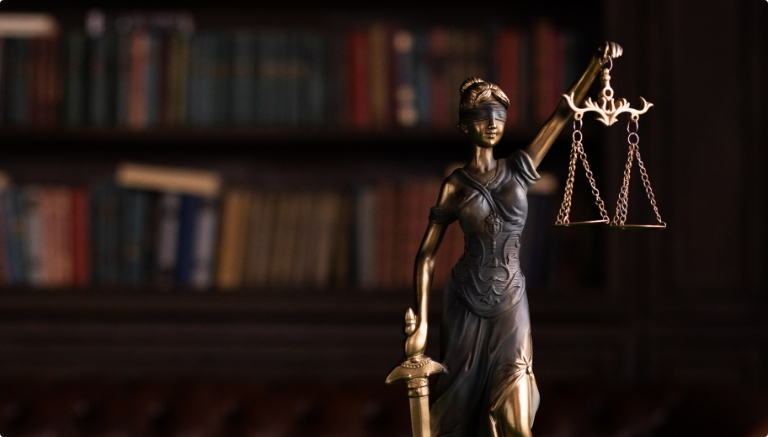 Statue of Lady Justice holding scales, with a blurred background of bookshelves.