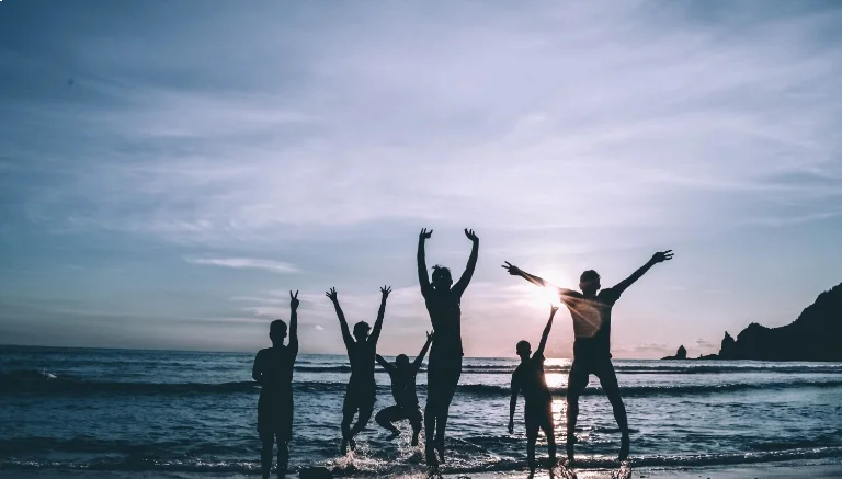 Silhouettes of people jumping and celebrating on a beach at sunset.