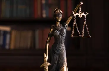 Statue of Lady Justice holding scales, with bookshelves in the background.